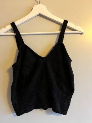 Svart stickad linnetopp från Twik - Svart stickad linnetopp från Twik med breda axelband och ribbad nederkant. Toppen har en enkel, clean design med mjuk stickad känsla och v-ringad hals. Perfekt att styla med jeans eller kjol för en chill look.