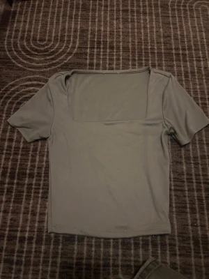 Grå topp med fyrkantig halsringning skims liknande  - Snygg grå topp med korta ärmar och en modern fyrkantig halsringning. Toppens stilrena design gör den enkel att matcha med olika outfits. Materialet känns mjukt och stretchigt, perfekt för dig som gillar en clean look.