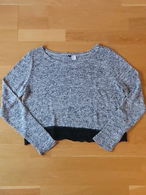 Gråmelerad croppad tröja - Gråmelerad långärmad tröja från H&M med svart spetskant nertill. Croppad modell med rund halsringning och mjukt, stickat material. Perfekt för dig som gillar en chill men ändå söt stil.