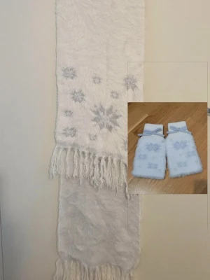 Set halsduk och fingerlösa vantar - Set med matchande halsduk och fingerlösa vantar. Färgen är vit med en kall ljusgrå färg