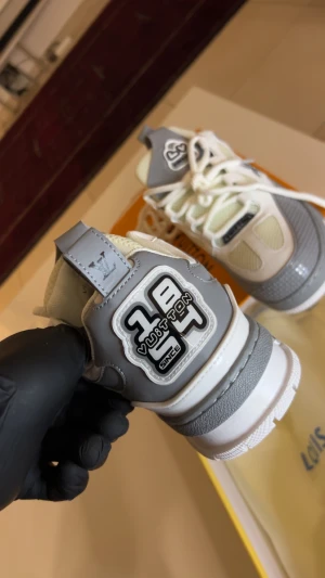 Louis Vuitton gråvita sneakers - Säljer ett par Louis Vuitton sneakers i vitt och grått med coola LV-detaljer och broderad logga på hälen. Skorna har meshpaneler, skinnpartier och tjocka vita snören. Snygg design med rund tå och platt sula, perfekt för dig som vill sticka ut med exklusiva sneakers.