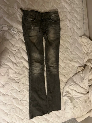 Grå bootcut jeans lågmidjade - Säljer ett par gråa Levi's jeans med bootcut och låg midja. Jeansen har slitningar och rå kant nedtill för en edgy vibe. Klassisk femficksmodell med dragkedja och knapp. Perfekt för dig som gillar en avslappnad och cool stil.