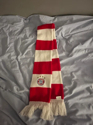 Bayern München halsduk - Tjena! Säljer denna schyssta halsduk med breda röda och vita ränder, broderat FC Bayern München-emblem och texten 'Mia san mia'. Halsduken har vita fransar i ändarna och är stickad i mjukt material, perfekt för att visa support på matchen. Släpper den från start vid 249 men går att ta ner i pris lite