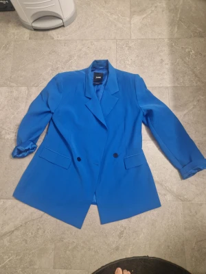 Blå kavaj från Pull&Bear - Snygg blå kavaj från Pull&Bear i storlek L. Dubbelknäppt med två framfickor och klassisk krage. Jackan har en stilren och modern look, perfekt för dig som vill sticka ut med färg. Materialet är mjukt och känns skönt mot huden. Fåtal gånger använd som ny.