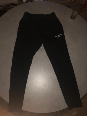 Svarta mjukisbyxor Björn Borg S - Svarta mjukisbyxor från Björn Borg med vit logga på vänster lår. Byxorna har snörning i midjan och är tillverkade i mjukt bomullsmaterial. Passformen är slim och benen är smalare nedtill. Perfekta för chill eller träning.