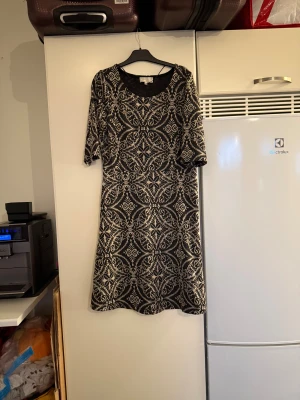 Svart och beige mönstrad klänning Cream - Snygg kortklänning från Cream i svart och beige med ett detaljerat, nästan barockinspirerat mönster. Klänningen har rund halsringning och trekvartsärm. Materialet känns mjukt och stretchigt, perfekt för dig som gillar unika prints och bekväm passform. Storlek M. Mycket fint skick, jag hittar inga synliga anmärkningar eller defekter. 
