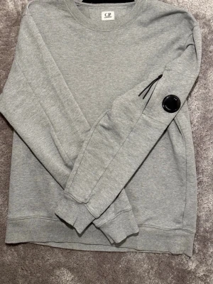 Grå sweatshirt från C.P. Company - Säljer en grå C.P. Company sweatshirt i nyskick, knappt använd. Inga skavanker förutom en liten repa på märket på armen. Tröjan är köpt direkt från C.P. Companys officiella hemsida. Perfekt för dig som vill ha en snygg och kvalitativ sweatshirt! Hör av dig vid intresse.😊