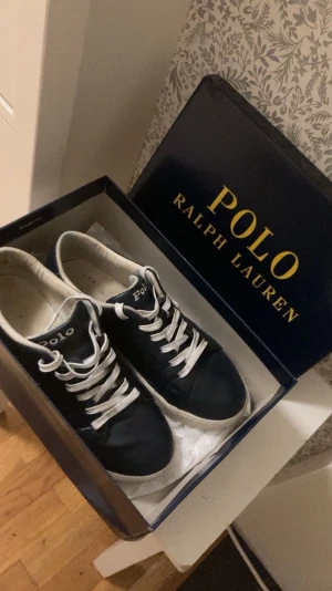 Polo Ralph lauren sutton navyblå - Snygga blåa sneakers från Polo Ralph Lauren med vit sula och vita snören. Klassisk låg modell med rund tå och Polo-logga på sidan och plösen. Skorna är tillverkade i skinn och har en stilren design som passar till jeans och hoodie.