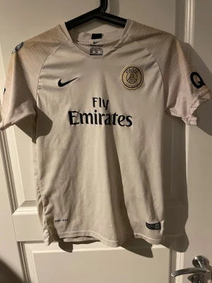 Psg tröja - Bilderna visar en PSG Neymar Jr matchtröja från Nike, inte skor. Tröjan är ljusbeige med svarta detaljer, Paris Saint-Germain-emblem och nummer 10 på ryggen.