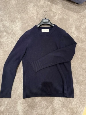 Mörkblå stickad tröja från A Day's March - Snygg mörkblå stickad tröja från A Day's March med rund hals och ribbade muddar vid ärmslut och nederkant. Perfekt för dig som gillar stilrena och klassiska plagg. Passar dig som vill ha en enkel men schysst look. Strl L