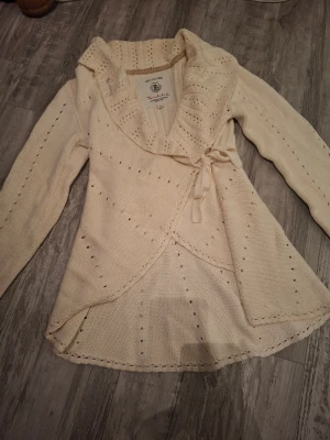 Bondelid vit stickad omlott tröja - Säljer en beige stickad omlottkofta från Bondelid med lång ärm och knytning i sidan. Koftan har hålstickade detaljer och bred krage. Bra skick och har andvänts få tal gånger. Storlek M men kan passa både som S och L därmed. Köptes för ca 700kr, priset kan förhandlas!
