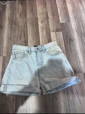 Ljusblå denimshorts med uppvik - Säljer ett par ljusblå denimshorts från lager 157 ”diba” med klassisk femficksdesign och uppvikta benslut. Shortsen har hög midja och är gjorda i bomull, perfekta för chill dagar när du vill ha en enkel och clean look.