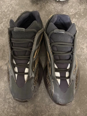 Adidas Yeezy 700 V3 svart/brun sneakers - Säljer ett par Adidas Yeezy 700 V3 sneakers i svart och brun med coola mönstrade paneler och chunky sula. Skorna har snörning och en futuristisk design med mesh och syntetmaterial. Perfekt för dig som vill sticka ut med din stil.