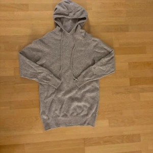 Beige stickad hoodie med huva och snörning - Mjuk och skön beige hoodie med huva och långa ärmar. Tröjan har snörning vid halsen och ribbade muddar vid ärmslut och nederkant. Perfekt för chill dagar och enkel att matcha med jeans eller mjukisbyxor.