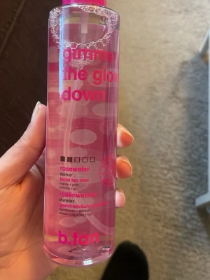 b.tan gimme the glow down face mist - Säljer en ansiktsmist med rosenvatten från b.tan, 'gimme the glow down'. Kommer i en genomskinlig rosa plastflaska med pump och rosa text. Ger fukt och glow till huden och har en lätt brun-utan-sol-effekt för ansiktet.