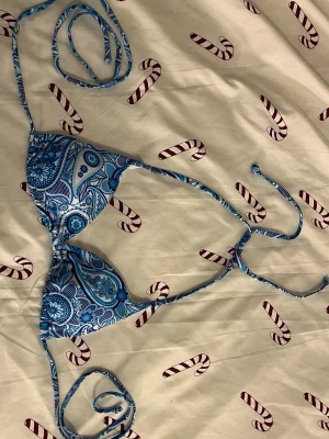 Blå mönstrad bikiniöverdel med snörning - Säljer en snygg bikiniöverdel med blått mönster och blommor. Modellen har trekantsformade kupor och långa snören för att knyta runt hals och rygg. 