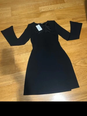 Svart kortklänning från Bikbok - Supersnygg svart klänning från Bikbok i storlek XS. Modellen är kort med långa trumpetärmar och har en stilren, figurnära passform. Materialet känns mjukt och stretchigt, perfekt för dig som gillar enkel men trendig design. Klänningen har en rund halsringning och är helt enfärgad.