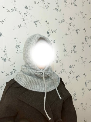 Ljusgrå stickad huva med snörning - Säljer en ljusgrå stickad huva med snörning framtill. Huvan har ribbad struktur och är gjord i ett mjukt material som sitter skönt runt halsen och huvudet. Perfekt för att hålla värmen och ge en cool vibe till din outfit.