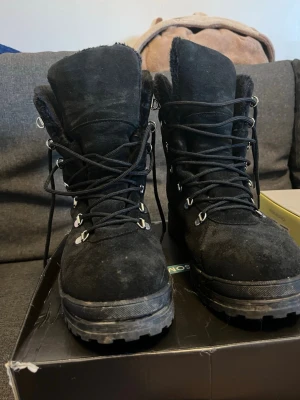 Svarta JOBI kängor i mocka, storlek 41 - Svarta kängor från JOBI i mocka med grov sula och snörning. Insidan är fodrad för extra värme och yttermaterialet är slitstarkt. Metallhakar för snörningen och robust mönstrad sula med röda detaljer undertill. Perfekt för kalla dagar och utomhusaktiviteter.