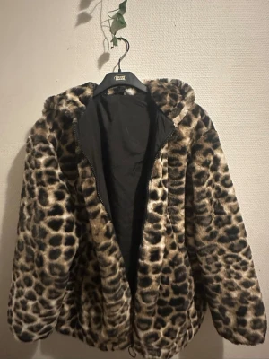 Leopardmönstrad pälsjacka med huva - Säljer en fluffig pälsjacka med leopardmönster och huva. Jackan har dragkedja framtill och är fodrad med svart tyg på insidan. Perfekt för dig som vill sticka ut och hålla dig varm under höst och vinter.