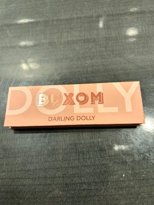 Buxom Darling Dolly ögonskuggspalett - Snygg ögonskuggspalett från Buxom med fem nyanser: matt beige, skimrande champagne, roséguld, guldbrun och djup röd. Paletten har en spegel och är i en stilren rosa förpackning. Perfekt för att skapa både mjuka och glittriga looks.