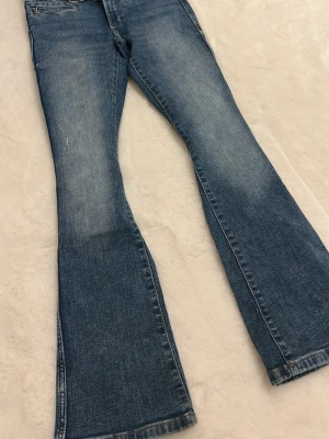 Blå bootcut jeans från H&M - Säljer ett par blå bootcut jeans från H&M med klassisk femficksdesign och snygga detaljer på bakfickorna. Jeansen har en lowwaist-passform och är gjorda i mjukt denimtyg med lätt tvättad look. Perfekta för dig som gillar retrostil och vill ha ett par jeans med lite extra sväng i benen. 🫰🏼