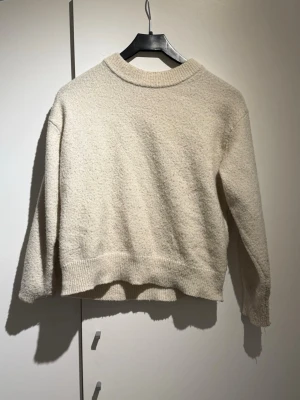 Beige stickad tröja från Gina Tricot - Mysig beige stickad tröja från Gina Tricot med rund hals och ribbade muddar vid hals, ärmslut och nederkant. Perfekt för lager-på-lager och chill dagar. Tröjan har en loose passform och långärmade ärmar.