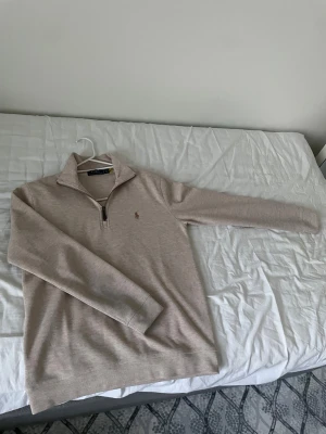 Beige half zip tröja från Polo Ralph Lauren - Säljer en beige långärmad tröja från Polo Ralph Lauren med half zip och klassisk krage. Tröjan har ett diskret broderat logotyp på bröstet och är gjord i mjuk bomull. Perfekt för chill höstdagar eller när du vill ha en clean look.