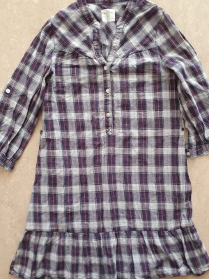 Skjortklänning - Säljer en rutig skjortklänning från H&M i storlek 34. Klänningen har långa ärmar med knappdetaljer, knappar framtill och volang längst ner. Färgerna är marinblå, vit och röd. Perfekt för dig som gillar avslappnad och cool stil.