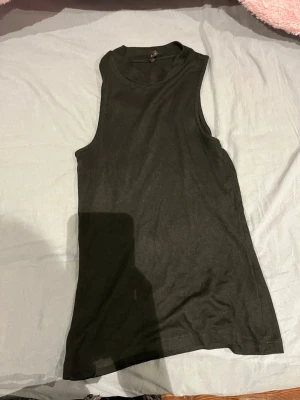 Svart ribbad ärmlös linnetopp - Säljer en svart, ribbad linnetopp från Gina Tricot i storlek S. Toppen är ärmlös med rund hals och har en slim passform. Perfekt att styla med jeans eller kjol för en enkel och clean look.