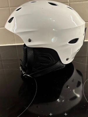 Skidhjälm  - Skidhjälm vit .  Produkten är tillverkad i hård plast med vadderad insida och justerbart hakband.