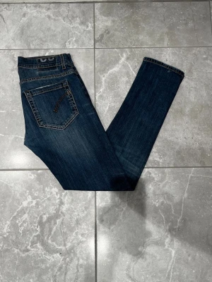 Dondup jeans - Dondup jeans i blå denim med raka ben och knappgylf. Jeansen har kontrastsömmar och en tidlös look som funkar till allt. Perfekt för dig som gillar stiliga jeans med autentisk känsla. Storleken är i 32.