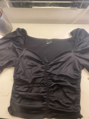 Svart croppad topp med puffärm - Säljer en svart croppad topp från Gina tricot med långa puffärmar och snygg snörning framtill. Toppen har en söt v-ringning och är gjord i glansigt, stretchigt material som sitter tight och markerar midjan.