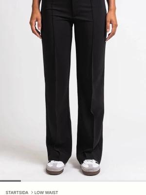 Svarta wide byxor från Madlady - Säljer ett par svarta wide byxor från Madlady med låg midja. Byxorna har raka ben och en stilren look som passar till sneakers. Materialet känns mjukt och har en snygg fall. Perfekt för dig som gillar bekväma byxor.