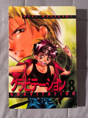 Gravitation 8 - En fartfylld manga om musik, kärlek och humor! Följ Shuichi och hans band Bad Luck när de kämpar med relationer, hemligheter och drömmar om en framtid i USA. Perfekt för dig som gillar romantik och skratt. Rekommenderas från 16 år.
