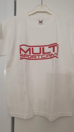 T-shirt - Vit t-shirt från Fruit of the Loom med röd MULTI SPORTCAMP-tryck både fram och bak. Klassisk rund hals och korta ärmar. Tillverkad i mjuk bomull, perfekt för sportiga aktiviteter eller chill dagar. Snygg och enkel design med tydlig logga.