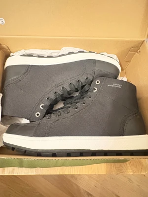 Svarta vattentäta boots från Linear - Svarta boots från Linear i vattentätt material med grov mönstrad sula för extra grepp. Skorna har snörning, rund tå och detaljer i syntet och textil. Vit mellansula ger en snygg kontrast. Perfekta för höst och vinter när du vill hålla stilen och fötterna torra.