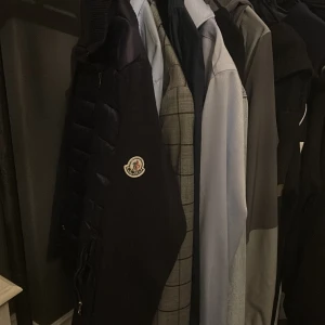 Svart Moncler pufferjacka herr - Snygg svart pufferjacka från Moncler med quiltad front och ärmar i mjukare material. Jackan har dragkedja framtill, två fickor med dragkedja och klassisk Moncler-logga på ärmen. Perfekt för dig som vill ha en stilren och exklusiv look.