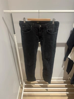 Lee jeans - Svarta jeans från Lee, modell Luke, med klassisk femficksdesign och smal passform. Jeansen har svarta sömmar, Lee-logga på bakfickan och är tillverkade i slitstarkt bomullsmaterial. Perfekt för dig som gillar en stilren och enkel look. Storlek är W33 och L34. Hör av er vid frågor eller funderingar 