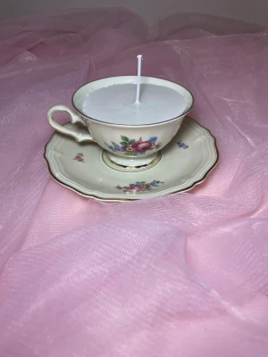 Doftljus i en tekopp i en vit kräm färg med flerfärgat blommigt mönster nr 2 - Det här ljuset är gjort av återanvändbara material. Tekoppen är köpt secondhand och stearinet är från kyrkor som tänkte slänga det. Det här ljuset har en svag doft utav vanilj, så känsliga även kan använda det. Det finns även fler ljus med denna design på hemsidan, om man vill köpa sets. 