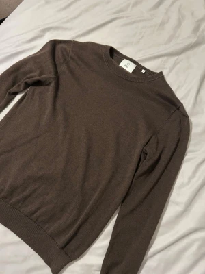 Brun stickad tröja från  BLÄCK - Säljer en enkel och stilren brun stickad tröja från BLÄCK. Tröjan har rund halsringning och långa ärmar, perfekt för lager-på-lager under kyliga dagar. Mjuk och skön kvalitet som passar till jeans eller kjol.