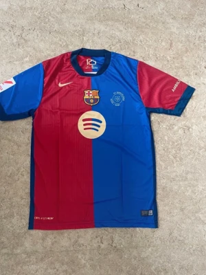FC Barcelona fotbollströja Lamine Yamal - Säljer en FC Barcelona matchtröja från Nike med Lamine Yamal och nummer 19 på ryggen. Tröjan har klassiska rödblå färger, klubbmärke och sponsortryck på bröstet samt UNHCR-logga på ryggen. Tillverkad i polyester med rund hals och korta ärmar.