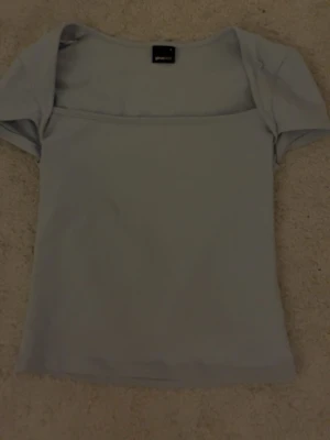 Ljusblå topp från Gina Tricot - Säljer en ljusblå topp från Gina Tricot i storlek S. Toppen har en fyrkantig halsringning och korta ärmar, med en slim passform som sitter snyggt på kroppen. Materialet är mjukt och stretchigt, perfekt för att styla med jeans eller kjol.