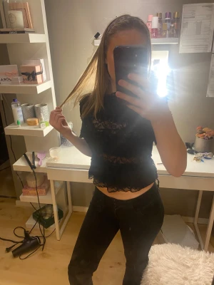 Svart spetsblus med volanger - Säljer en svart blus med genomskinlig spets och volangdetaljer. Blusen är croppad och har korta ärmar. Perfekt för dig som gillar en lite edgy och trendig stil. Materialet är lätt och luftigt, vilket gör den skön att bära. Passar till både jeans och kjol.