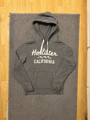 Grå Vintage Hollister Hoodie - Säljer denna feta grå hollister hoodien, sällsynt och svår att få tag på! | Storlek S | Väldigt bra skick, endast lite gul färg på snöret se bild 4 | Modell 175cm, 68kg | Hör av vid ytterligare frågor! | Pris diskuterbar vid snabbr köp!