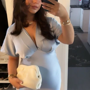 Ljusblå långklänning i satin - Superfin ljusblå långklänning i satin med v-ringning och korta ärmar ifrån ZARA. Klänningen har en elegant omlottkänsla upptill och faller snyggt längs kroppen. Perfekt för dig som vill ha en stilren och trendig look till sommaren, balen, bröllop eller event. St L men passar mig som vanligtvis bär M. Är 159cm.