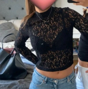 Svart spetsblus  - Säljer en svart, långärmad blus storlek S. Oklart vart den är köpt. Blusen är croppad och har ett genombrutet spetsmaterial med blommigt mönster. Hög hals och figurnära passform. Köpt förra året och använts några gånger men inget fel på tröjan