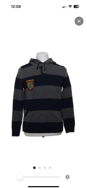 Stickad hoodie  - Randig hoodie från Henry Cotton’s University Stilren hoodie i grått och mörkblått med breda ränder. Klassisk modell med huva och magficka framtill. Broderade patches på bröstet och ärmen som ger en preppy/university-känsla. Mjuk och bekväm, perfekt till vardags eller skola. Passar även M.