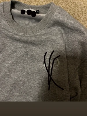 Grå sweatshirt med broderad logga -  Fråga gärna efter mer bilder så får ni de i chatten. Helt ny lappen kvar. Storlek M med ett skönt material innuti. Passar väl till vintern
