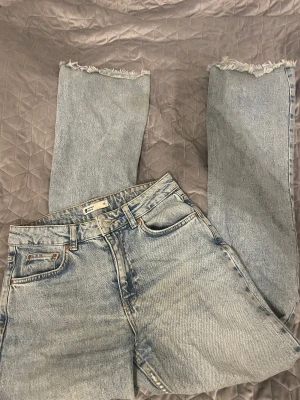 Ljusblå jeans  - Säljer ett par ljusblå wide jeans  med hög midja och rå, fransad kant längst ner på benen. Klassisk femficksmodell och snygg tvättad look. Perfekt för dig som gillar avslappnad stil och vill ha ett par jeans som sticker ut.